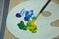 The artist mixes with a brush the colors of paints for painting on a palette. Palette with paints in hand close-up Royalty Free Stock Photo