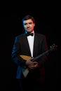 Artist musician, a dark-haired man in a black suit and a bow tie, plays a balalaika Royalty Free Stock Photo