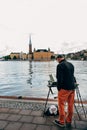 Artist painting the cityscape of the Riddarholmen Island and Gamla Stan by the sea in Stockholm