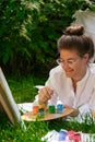 Artist painting on the easel outdoors in the garden. Open air outdoor art workshop. Draw on the canvas with brush and Royalty Free Stock Photo