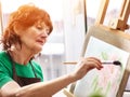 Artist painting easel in studio. Authentic senior woman.