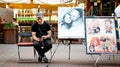 An artist with paintings sits on the street and waits for customers