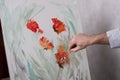 An artist with a palette knife paints red flowers on a white canvas Royalty Free Stock Photo