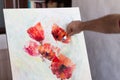 An artist with a palette knife paints red flowers on a white canvas Royalty Free Stock Photo