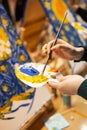 Artist`s hand dips a brush into a palette with yellow and blue paint. Clouse-up