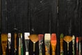 Artist`s tools, brushes in paint are in a row on a black wooden background.