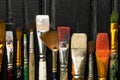 Artist`s tools, brushes in paint are in a row on a black wooden background. Royalty Free Stock Photo