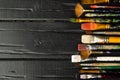 Artist`s tools, brushes in paint are in a row on a black wooden background. Royalty Free Stock Photo