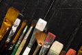 Artist`s tools, brushes in paint are in a row on a black wooden background. Royalty Free Stock Photo