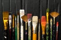 Artist`s tools, brushes in paint are in a row on a black wooden background. Royalty Free Stock Photo