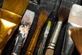 Artist`s tools, brushes in paint are in a row on a black wooden background. Royalty Free Stock Photo