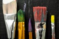 Artist`s tools, brushes in paint are in a row on a black wooden background. Royalty Free Stock Photo