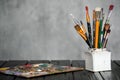 Artist`s tools, brushes, paints and a palette lie on a black wooden table on a gray fabric background. Royalty Free Stock Photo