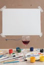 Artist's workplace. Paints and brushes, palette and easel. Blank sheet of paper. Among all this, there is a glass of red