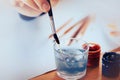 The artist washes the brush in a glass of water, washing off the blue gouache from it. Drawing on a white sheet of paper. Royalty Free Stock Photo