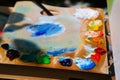 Artist wooden palette, blurred mess of fresh bright colorful oil paints mixed in disorder, outdoor painting plein air Royalty Free Stock Photo