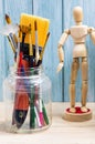 Artist workspace, assorted of brush in an old glass jar on wooden tabletop with human model