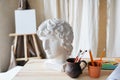 Artistic brushes , clay ancient head model, palette and drawing supplies. Horizontal photo of old wooden table in art studio.