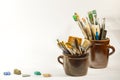 Artistic brushes colorful nice stones and painting tools in old ceramic pots on a white background