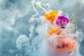 Artistic close-up of a refreshing cocktail adorned with vibrant edible flowers amidst swirling mist