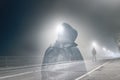 An artistic double exposure of a lone hooded figure standing in the middle of a country road below a street light on a spooky nigh