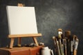 Artistic equipment in a artist studio: empty artist canvas on a wooden easel, paint tubes and paint brushes Royalty Free Stock Photo
