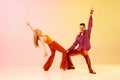 Artistic, expressive couple, man and woman emotionally dancing disco dance against gradient pink yellow background