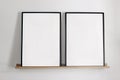 Artistic mockups template. Two black vertical picture frames on bamboo wooden shelf. White wall background. Posters at