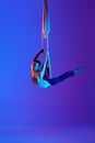 Artistic performance. Young man, acrobat training with aerial ribbons, doing gymnastics tricks against gradient blue