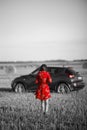Artistic picture of a woman in a red dress on a field walking towards a car Royalty Free Stock Photo