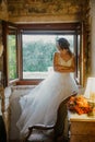 Artistic processing Fantasy girl princess in WHITE WEDDING dress stands in medieval CASTLE room looking vintage window Royalty Free Stock Photo