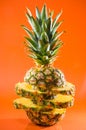 Artistic sliced, standing pineapple on orange background, vertical shot