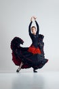 Artistic woman, flamenco dancer n striking black and red dress performing with passion, dancing against grey studio