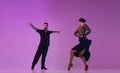 Artistic young man and woman, professional dancers in stylish stage costumes performing tango over purple background on Royalty Free Stock Photo