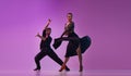 Artistic young man and woman, professional dancers in stylish stage costumes performing tango over purple background on Royalty Free Stock Photo