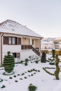 Artistically trimmed green bushes in the snow-covered yard of a cozy two-story cottage Royalty Free Stock Photo