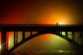 Artwork decoration. Silhouette of powerful metallic bridge at night with foggy backlight. Silhouette of person standing on bridge