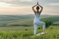 Woman practices yoga tree pose at dawn in green fields