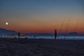 As these men fish on the beach with multiple rods at dusk, the full supermoon is visible over the town of Rethymno, Crete, Greece Royalty Free Stock Photo