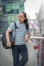 Asain / Thai-Chinese long black hair guy with blue line t-shirt is thinking and holding backpack on his sholder near the sky train