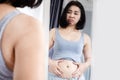 Asain woman checking her abdominal and looking at her fat belly in a mirror, weight gain concept Royalty Free Stock Photo