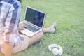 Asain woman wearing a shirt sitting on the green grass while typing Thai keyboard of laptop put on the leg with the ear plug for r Royalty Free Stock Photo