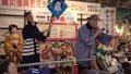 Pan left video of Japanese women in kimono and men in happi jacket doing an auction at the Tori-no-Ichi Fair of Ootori shrine.