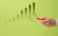 Ascending bar chart and hand with red magnifying glass. Data analysis, green background Royalty Free Stock Photo
