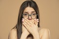 Ashamed woman with hand over mouth on a beige background