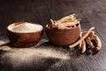 Ashwagandha root and powder in wooden cups on dark background.