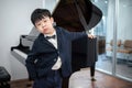 Asia boys wearing suit standing next to the grand piano and put his hand in his pants pocket at the school. Feeling boring on the