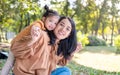 Asia daughter riding her mother back in the park with copy space. Family outdoor activity. Mom and kid smile and looking at the Royalty Free Stock Photo