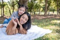 Asia daughter riding mother back and lying on the ground in the public garden under sunlight with copy space. The cute girl is Royalty Free Stock Photo
