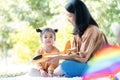 Asia daughter sitting on the floor and looking at the camera with mom in the park. Family outdoor activity. Mom talks with kid and Royalty Free Stock Photo